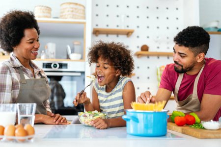 Photo for Overjoyed young african american family with kid have fun cooking at home together, happy smiling parents enjoy weekend play with child in kitchen - Royalty Free Image