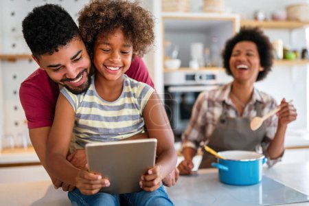 Téléchargez les photos : Heureuse famille afro-américaine s'amuser avec l'appareil à la maison. Les parents noirs et l'enfant en utilisant une tablette numérique - en image libre de droit