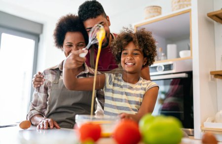 Foto de Feliz afroamericana sonriente familia preparando comida saludable en la cocina, divirtiéndose juntos el fin de semana - Imagen libre de derechos
