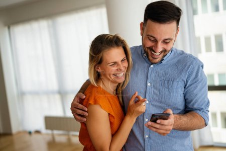 Photo for Smiling young couple embracing while using a smartphone. People sharing social media on mobile phone. - Royalty Free Image