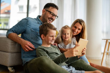 Téléchargez les photos : Joyeux jeune famille s'amuser à la maison. Parents avec enfants utilisant une tablette. Les gens aiment le concept de bonheur. - en image libre de droit