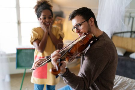 Foto de La música es muy divertida. Padre joven enseñando a su hija a tocar el violín y sonreír. Concepto de felicidad del niño padre. - Imagen libre de derechos