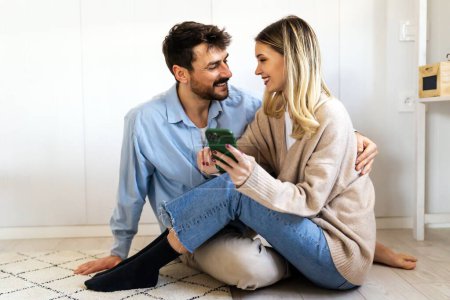 Foto de Sonriendo joven pareja abrazando mientras mira el teléfono inteligente. Pareja multiétnica compartiendo redes sociales en el teléfono inteligente. - Imagen libre de derechos