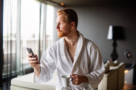 Photo for Happy smiling man relaxing while looking at mobile phone. Closeup of man using smartphone to checking email at home. Man reading news on smartphone - Royalty Free Image