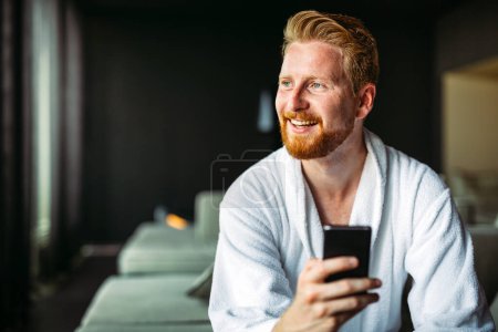 Photo for Happy smiling man relaxing while looking at mobile phone. Closeup of man using smartphone to checking email at home. Man reading news on smartphone - Royalty Free Image