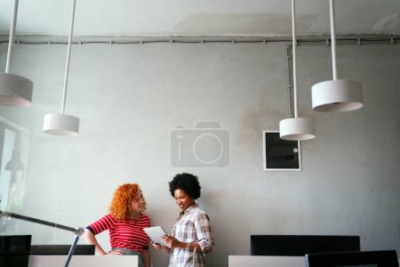 Photo for Two businesswoman working together using digital tablet pc and talking about a business project. Small creative diversity team of females executives meeting work in office. - Royalty Free Image
