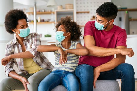 Téléchargez les photos : Jeune famille afro-américaine portant des masques médicaux protecteurs au milieu de la pandémie de coronavirus à la maison - en image libre de droit