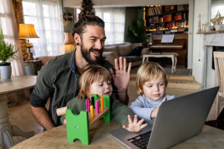 Photo for Happy single father with children waving hands while doing video call through laptop at home. People, family technology communication concept - Royalty Free Image