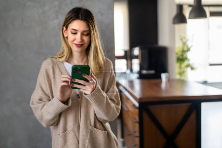 Young girl wearing sweater using smartphone at home, communication and social network concept, woman browsing the internet