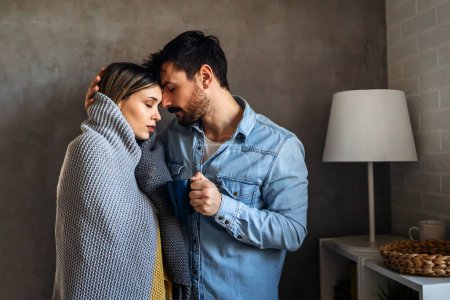 Photo for Freezing couple covered with a cozy blanket. Man and a woman wrapped in a warm blanket in a cold room. - Royalty Free Image