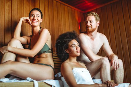 Téléchargez les photos : Profiter d'une journée de soins. Groupe de personnes heureuses multiethniques, amis se relaxant dans le sauna ensemble. - en image libre de droit