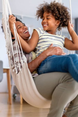 Téléchargez les photos : Portrait de femme noire heureuse et sa fille préadolescente mignonne s'amusant ensemble à la maison, Happy afro-américaine lien de famille, embrasser et sourire - en image libre de droit