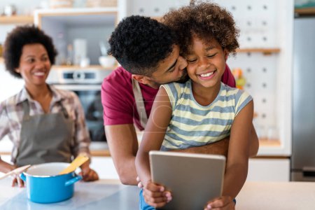 Téléchargez les photos : Heureuse famille afro-américaine s'amuser avec l'appareil à la maison. Les parents noirs et l'enfant en utilisant une tablette numérique - en image libre de droit