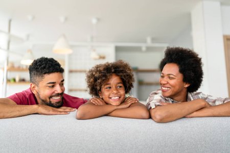 Happy biracial girl smiling with young multiracial parents enjoy weekend at home together, overjoyed multiethnic daughter play with loving mom and dad
