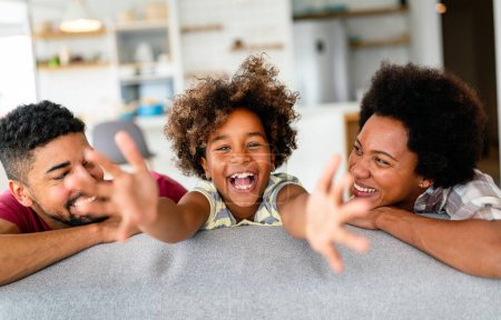 Téléchargez les photos : Portrait d'une jeune famille afro-américaine souriante avec une petite fille adolescente assise sur un canapé à la maison profiter du week-end ensemble. - en image libre de droit