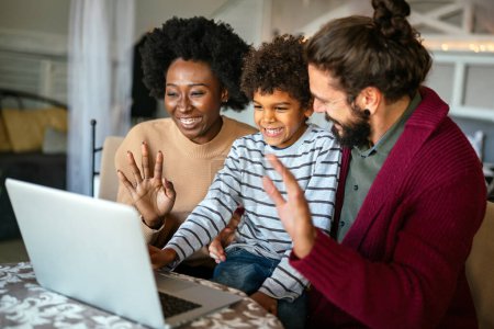 Photo for Happy diverse multiethnic family gathering around laptop and having fun during a video call at home. Multi ethnic parents enjoying quality time with child while using digital device. - Royalty Free Image