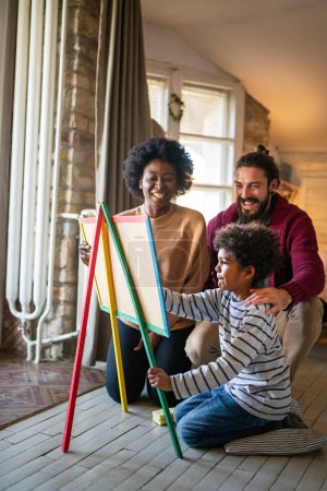 Photo for Happy bonding multiethnic african american family drawing on black board with colored chalk. Smiling mixed race parents enjoying creative hobby activity with little son. - Royalty Free Image