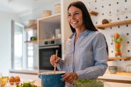 Foto de Retrato de una mujer en la cocina de su casa para la salud, la dieta o la nutrición. Sonríe, come y cocina con una hembra feliz comiendo sano - Imagen libre de derechos