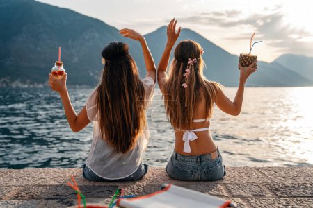 Téléchargez les photos : Filles heureuses s'amuser à boire des cocktails sur la plage pendant les vacances d'été. Les gens voyagent concept amusant - en image libre de droit