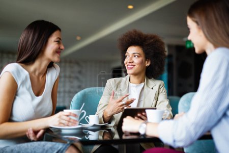 Photo for Woman and her clients discuss business ideas and collaborate over coffee in a cafe. Happy business partners using a digital device as they engage with each other in a lunch meeting. - Royalty Free Image