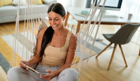 Young woman using digital tablet at home, female user holding pad computer looking at screen reading e-book app online relax on leisure with device work study online on couch