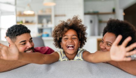 Happy biracial girl smiling with young multiracial parents enjoy weekend at home together, overjoyed multiethnic daughter play with loving mom and dad