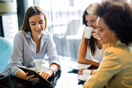 Photo for Woman and her clients discuss business ideas and collaborate over coffee in a cafe. Happy business partners using a digital device as they engage with each other in a lunch meeting. - Royalty Free Image