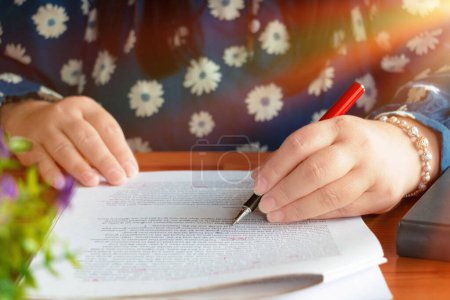 hand holding red pen over blurred paperwork on wooden table in office for proofreading concept
