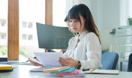 Téléchargez les photos : Focalisé asiatique femme employée travaillant avec document et ordinateur portable au bureau de l'entreprise. - en image libre de droit