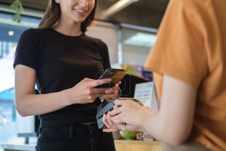 Foto de Smiling female customer using smart phone scan QR code for payment at coffee shop. NFC contactless payment concept. - Imagen libre de derechos