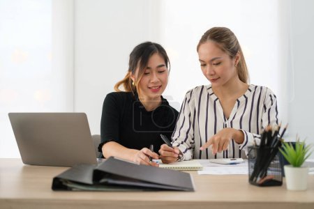 Téléchargez les photos : Sourire asiatique femme employé pointant sur notepad et expliquer nouvelle idée à ses collègues. - en image libre de droit