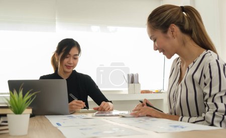 Téléchargez les photos : Des jeunes femmes entrepreneures souriantes discutent des idées de projet tout en étant assis dans un bureau moderne lumineux. - en image libre de droit