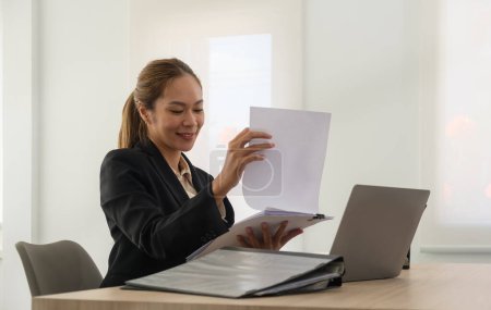 Téléchargez les photos : Charming female entrepreneur in black suit working with document and using laptop at her workstation. - en image libre de droit