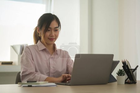 Téléchargez les photos : Jolie employée asiatique utilisant un ordinateur portable à son bureau. Mode de vie, technologie et communication sans fil. - en image libre de droit