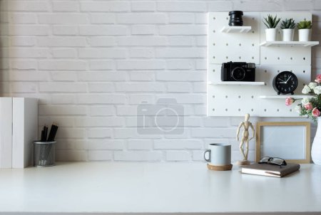 Foto de Creative workplace with books, picture frame, retro camera and coffee cup on white table. Copy space for text. - Imagen libre de derechos
