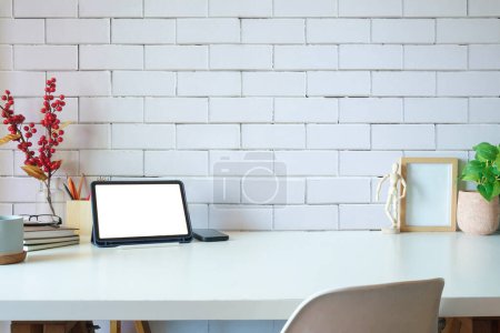 Foto de Comfortable workplace with digital tablet, picture frame, books and houseplant on white table. - Imagen libre de derechos