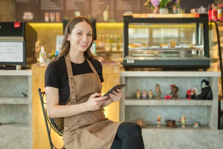 Photo for Smiling caucasian female coffee shop owner sitting in front of counter and receiving online order on digital tablet. - Royalty Free Image