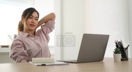Photo for Satisfied young businesswoman stretching her arms in the air, relaxing at workplace. - Royalty Free Image