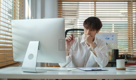 Téléchargez les photos : Focalisé asiatique homme économiste en chemise blanche regardant moniteur d'ordinateur, de travail dans le bureau moderne. - en image libre de droit