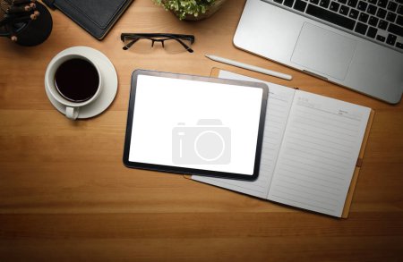 Photo for Top view of digital tablet, coffee cup, eyeglasses and notebook on wooden working desk. - Royalty Free Image