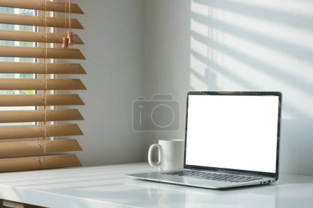 Foto de Ordenador portátil con pantalla vacía y taza de café en la mesa blanca en el interior de la oficina brillante. - Imagen libre de derechos