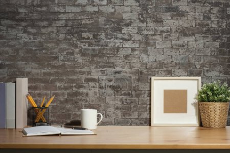 Photo for Blank picture frame, coffee cup, notebook and potted plant on wooden table. Stylish working space, home office. - Royalty Free Image