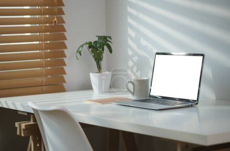 Téléchargez les photos : Intérieur moderne de bureau à domicile avec ordinateur portable, tasse de café et plante d'intérieur sur bureau blanc. - en image libre de droit