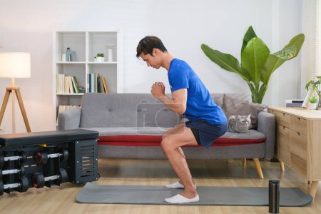 Téléchargez les photos : Homme en forme athlétique en vêtements de sport faire des exercices de squat à la maison. Style de vie sportif et concept de musculation. - en image libre de droit