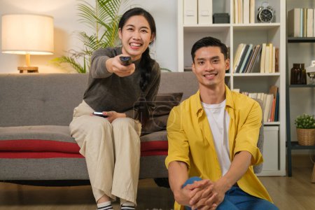 Téléchargez les photos : Joyeux jeune couple asiatique regarder la télévision ensemble dans le salon confortable. Les gens et le concept de loisirs. - en image libre de droit
