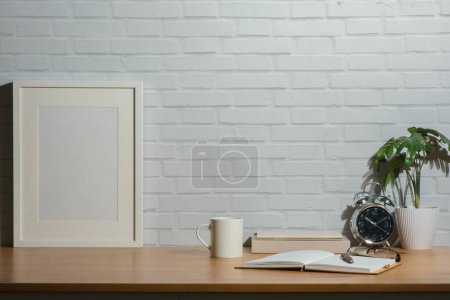 Photo for White empty frame mock up coffee cup, notebook and potted plant on wooden table in bright room of modern house. - Royalty Free Image