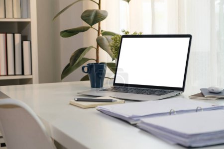 Foto de Ordenador portátil con pantalla en blanco, documentos contables, taza de café y suministros de oficina en la mesa blanca. - Imagen libre de derechos