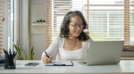 Photo for Portrait of middle age woman sitting at cozy home interior working on laptop with a happy face. - Royalty Free Image