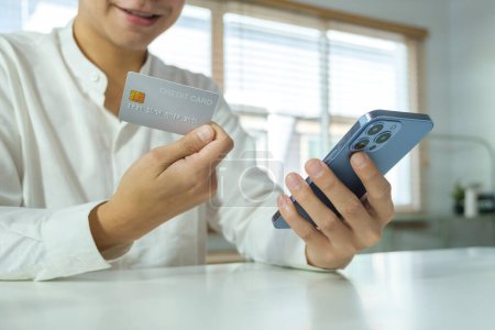 Téléchargez les photos : Heureux homme asiatique adulte tenant la carte de crédit et en utilisant le téléphone mobile, payer la facture avec paiement en ligne via Internet. - en image libre de droit