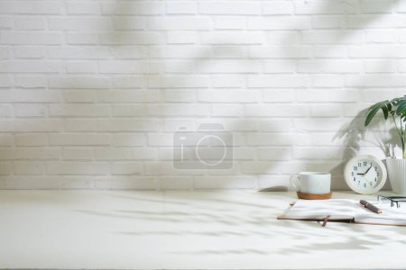 Foto de Cómodo lugar de trabajo con libros, reloj y taza de café en la mesa blanca contra la pared de ladrillo. - Imagen libre de derechos